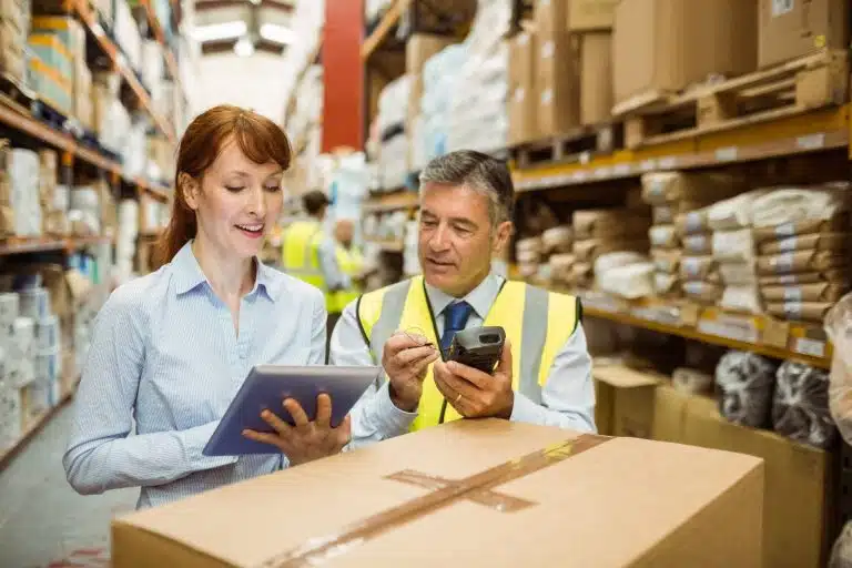 Two professionals using tablet and scanner in warehouse with inventory shelves