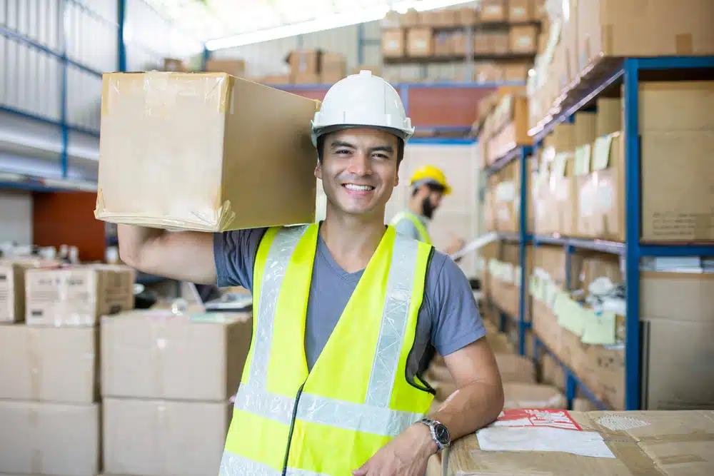 Warehouse worker in safety vest carrying box in organized distribution center