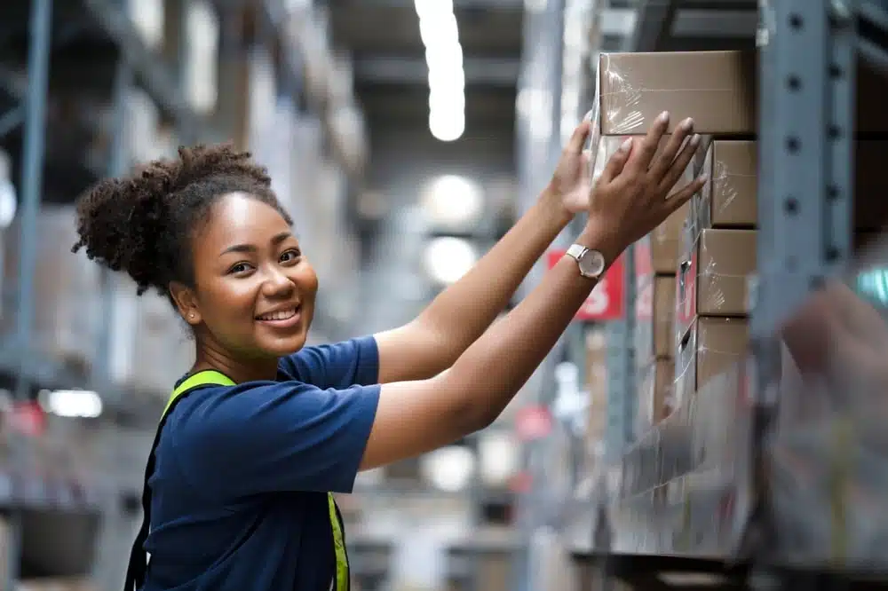 Smiling warehouse worker organizing inventory boxes on storage shelves