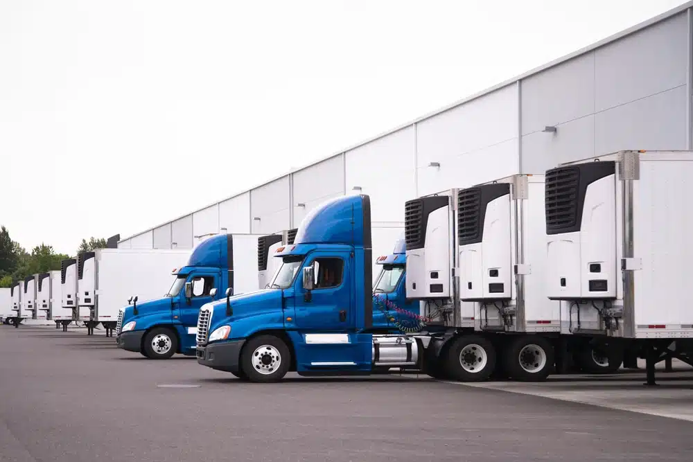 Blue semi-trucks with refrigerated trailers parked at warehouse loading docks