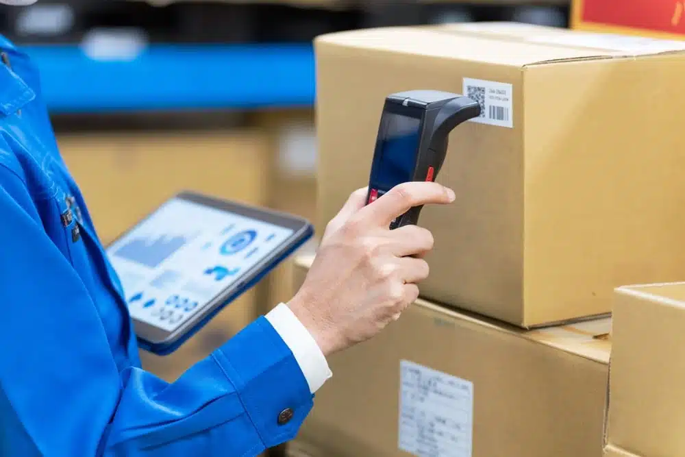 Warehouse worker scanning barcode on package with handheld scanner and tablet