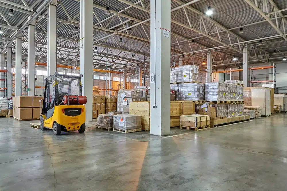 Yellow forklift moving pallets in large warehouse shipping and receiving facility