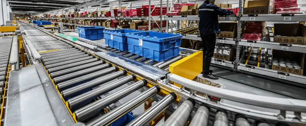 Warehouse worker in high-visibility vest walking past colorful storage crates and delivery truck