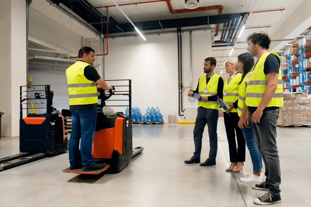 Warehouse workers in safety vests receiving forklift training in modern distribution center