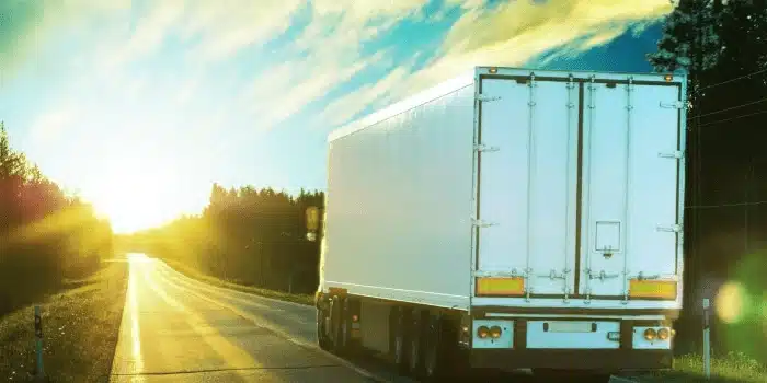 White semi-truck trailer driving on highway at sunset representing sustainable supply chain transportation
