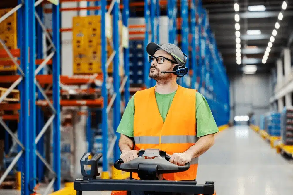 Warehouse worker in safety vest operating picking equipment in distribution center
