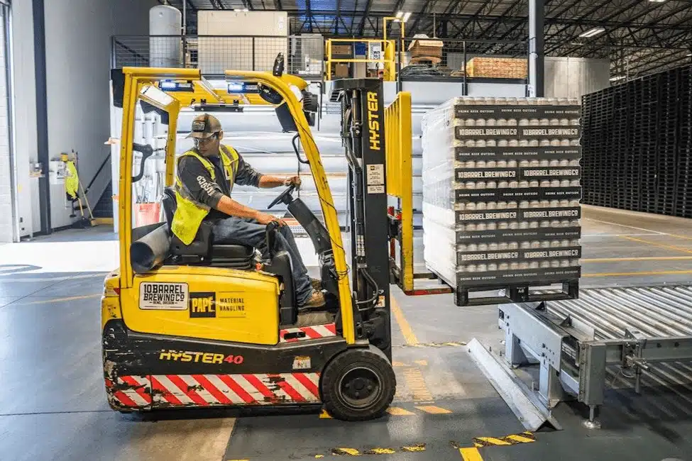 Warehouse worker operating yellow Hyster forklift moving pallets in cross docking facility