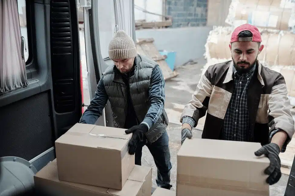 Two warehouse workers unloading cardboard boxes from delivery truck for cross docking