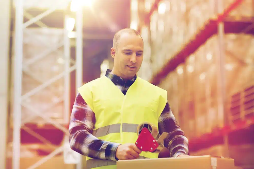 Warehouse worker in safety vest packing shipping box with protective dunnage materials