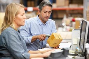 Man scanning box barcode; woman looking at computer screen