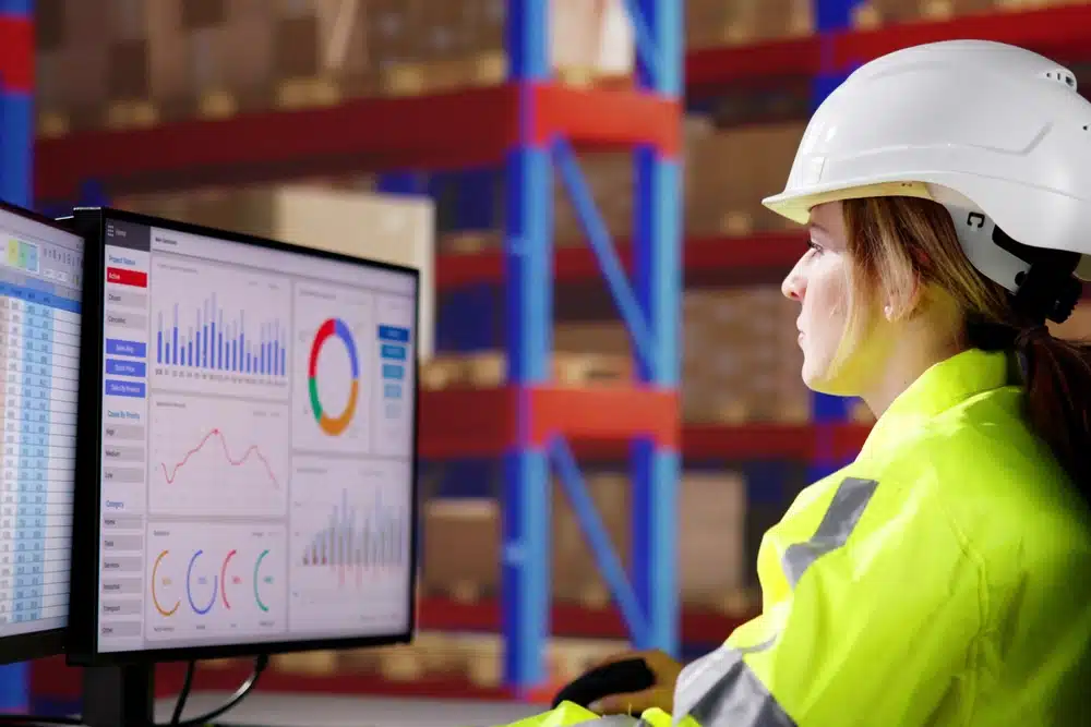Female warehouse manager analyzing KPI dashboard with charts and metrics on computer monitor