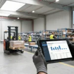 hands holding a tablet checking inventory with warehouse processes being shown in the background