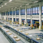 Logistics warehouse at dusk with automated belts and workers loading trucks for expedited shipping.